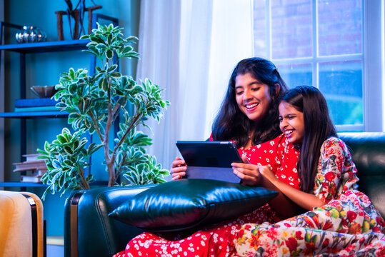 Indian little girls laugh together watching funny video on tablet while relaxing on the sofa - Powered by Adobe
