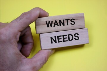 Hands holding wooden blocks with text 'wants' and 'needs' symbolizing decision making and priorities isolated on yellow background