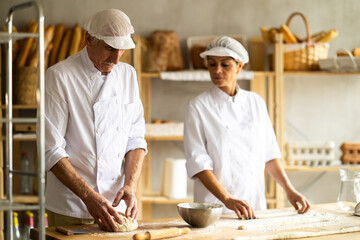 Elderly male chef and female skillfully kneads dough to bake delicious bread and croissants