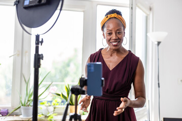 Smiling beautiful woman vlogging using her mobile phone at home
