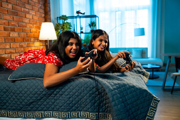Indian little girls gaming together while lying on bed and enjoying playful bonding time indoors
