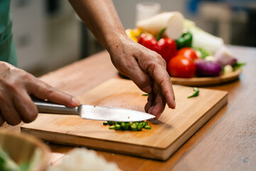Closeup of male hands slicing pepper on a wooden board in the kitchen, preparing to cook.