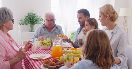 Happy big family of three generations having dinner together at home. Cheerful parents, grandparents and children sitting around table full of different food, passing dish in circle from hand to hand. - Powered by Adobe