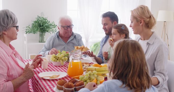 Happy big family of three generations having dinner together at home. Cheerful parents, grandparents and children sitting around table full of different food, passing dish in circle from hand to hand.