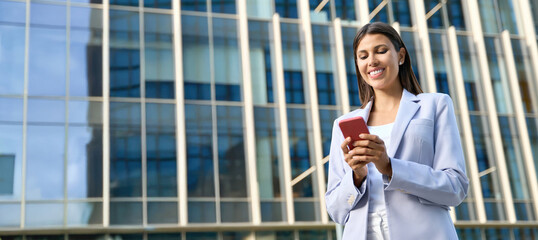 Latin hispanic business woman using smartphone cellphone financial trading app. Indian, middle eastern female entrepreneur businesswoman holding mobile cell phone for work outdoor. Banner, copy space