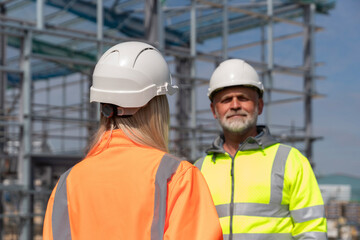 Two construction workers in bright safety jackets engage in conversation on a building site