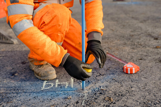 Close-up of construction worker measuring distance with tape measure and applying color tape on steel pin to mark road level