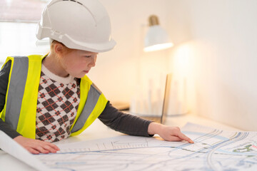 Young child engaged in a creative building activity in bright room while wearing safety helmet and vest during a learning session about architecture