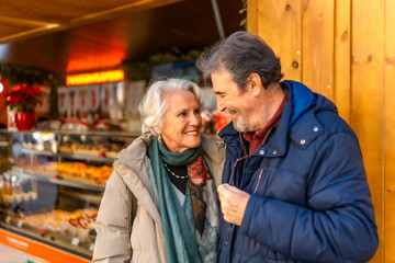 Obraz premium Happy senior couple smiling at christmas market in winter