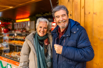 Happy senior couple smiling at christmas market in winter