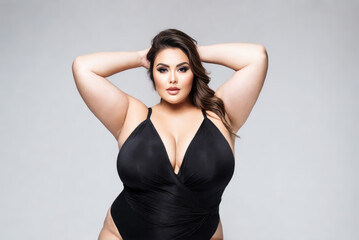 Fototapeta premium Sexy plus size fashion model in black one-piece swimsuit, fat woman in lingerie on gray background, body positive concept