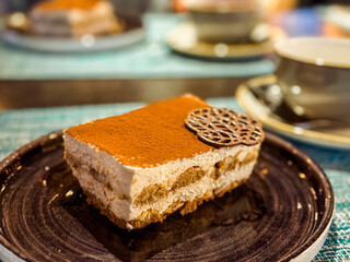Closeup of tiramisu dessert with cocoa powder and chocolate decoration on plate. Sweet indulgence, lifestyle, and hospitality with focus on food, taste, and culinary enjoyment.