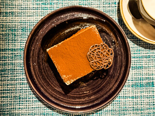 Closeup of tiramisu dessert with cocoa powder and chocolate decoration on plate. Sweet indulgence, lifestyle, and hospitality with focus on food, taste, and culinary enjoyment.
