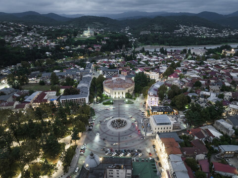 Aerial view of the illuminated Colchis Fountain and the Semenovsky Church stand out against the dark, mountainous backdrop, Kutaisi, Imereti, Georgia.