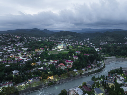 Aerial view of the Bagrati Cathedral perched atop Ukimerioni Hill, illuminated against the twilight sky, casting a serene glow over the Rioni River, Kutaisi, Imereti, Georgia.