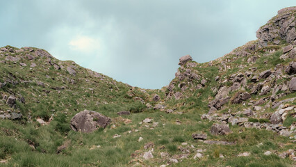 This captures a view looking up through the Gap of Dunloe. The rocky terrain is covered with green grass, creating a rugged landscape. It is located in County Kerry, Ireland.