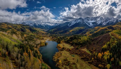 Aerial view of a lake nestled between colorful autumn forests and majestic, snowy mountains