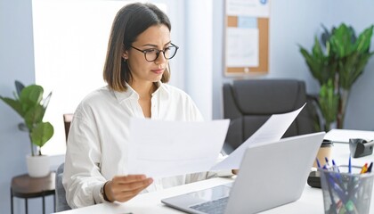 Focused businesswoman in office examines financial documents. A woman analyzes papers near laptop, desk in office setting