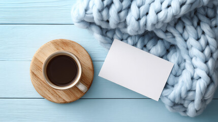 Flat lay with cup of coffee, wooden board, blank card, and soft knitted blanket on blue wooden background for cozy winter and autumn design mockups