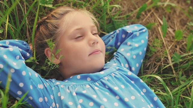 little girl child lies on the grass in the park. happy family kid dream concept. baby girl in fun the park lies on her back looks at the sky portrait close-up. girl in nature smiling portrait