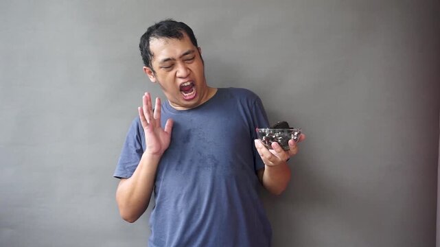 Footage of asian man show awfull eat chocolate cake on isolated grey background