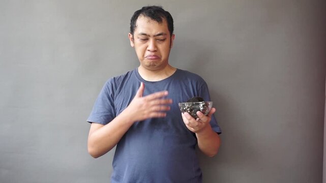 Footage of asian man show awfull eat chocolate cake on isolated grey background