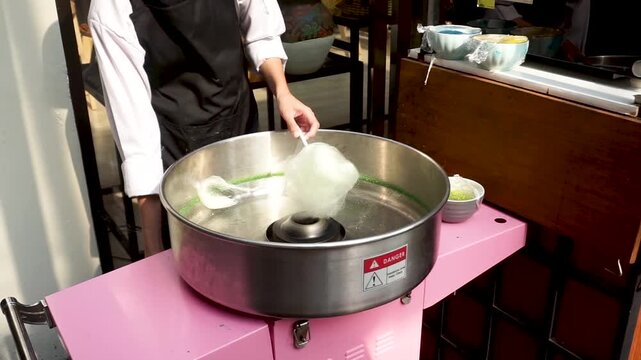 Close-up of a confectioner pouring granulated sugar into a commercial candy floss machine to create a fluffy sweet confection