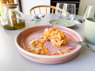 Partly eaten pastry on a pink ceramic plate with a fork placed on a cafe table near glass teapot and cups. Food, dining and lifestyle symbolizing refreshment, hospitality and leisure.