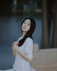 Elegant woman in white outfit posing gracefully by the water.