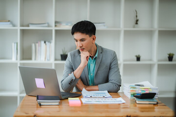 Businessman analyzing financial documents and using laptop computer working in office