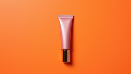 A pink cosmetic tube with a gold cap isolated on a vibrant orange background in a studio setting