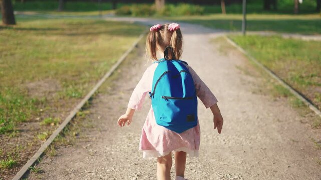 back to school. a little girl with a backpack runs through the green park to school along the path. education kid dream concept. a small sun child with a backpack back view runs the park to school