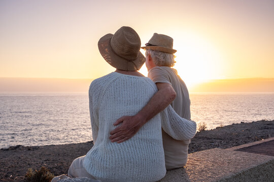 Back view of serene couple of seniors sitting face the sea at dusk, elderly caucasian people looking at horizon over water enjoying vacation or retirement