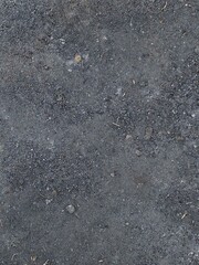 A vertical shot of a dark gravel and dirt surface, showing a rough, rocky texture with scattered pebbles and dust.