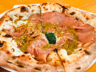 Freshly baked pizza with mortadella, pesto, pistachio, and basil on wooden table close-up. Food culture, dining, and culinary tradition expressed through italian cuisine and gourmet lifestyle.