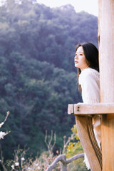 Naklejka premium A woman in a cozy white sweater gazes thoughtfully into the distance in a serene outdoor setting.