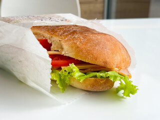 Fresh sandwich with lettuce, tomato, cheese, and ham wrapped in paper on table. Nutrition, lifestyle, and fast food expressed through diet, snack, and consumer culture.