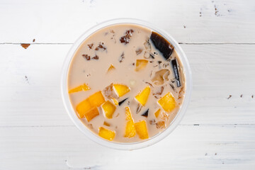 top view bowl of milktea flavor syrup mixed with grass jelly and mangoes and peach gum and tapiocas and red beans and guiling jelly etc. at vertical composition