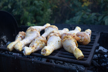 Backyard barbecue scene with racks of chicken drumsticks over hot coals and rising smoke; ideal for lifestyle, event, hospitality and seasonal food marketing emphasizing warmth and conviviality