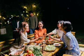 Friends sharing food, laughing and enjoying garden party at night