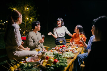 Asian friends enjoying garden party with barbecue and drinks at night
