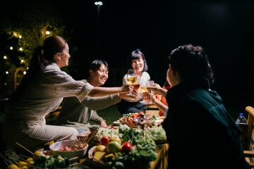 Asian friends toasting wine glasses during a night party in the garden
