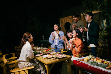 Friends clapping and enjoying barbecue dinner party in backyard