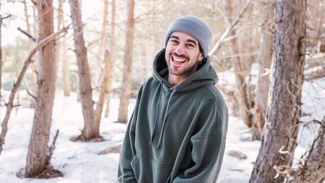 Young man smiling in snowy forest wearing hoodie and beanie