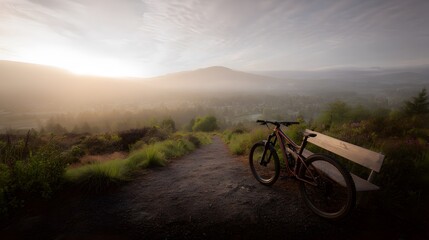Obraz premium Wide view of a mountain bike near trail in valley with misty peaks and sunrise glow