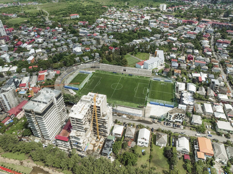 Aerial view of the vibrant green football field stands out amidst the urban sprawl and modern architecture, a stark contrast against the aged buildings, Constanta, Romania.