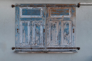 Old wooden shutters with peeling blue and white paint showing age and weathering on building exterior