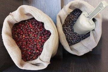 Dried black currant berries and dried rose hips in canvas bags with a scoop. Brown wooden background. Top view.