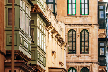 Traditional Maltese wooden balconies painted in vibrant colors on limestone facades, typical...