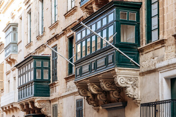 Traditional Maltese wooden balconies painted in vibrant colors on limestone facades, typical...